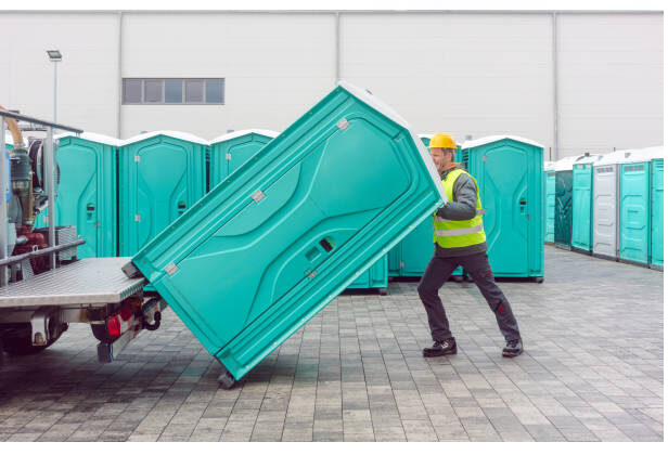Crew member loading a teal portable restroom unit onto a delivery trailer